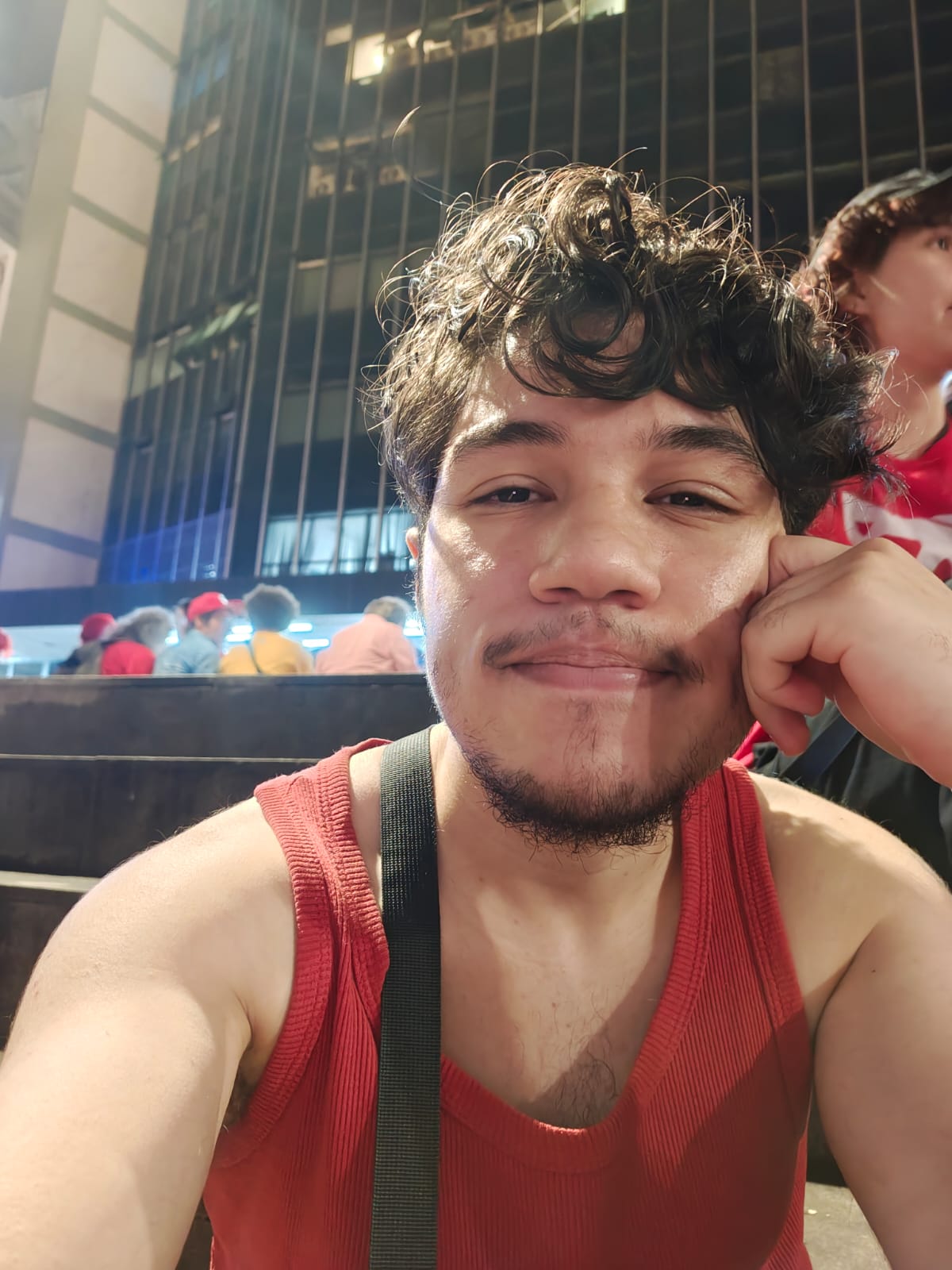Night selfie of me in a red tank top, resting my face on my hand