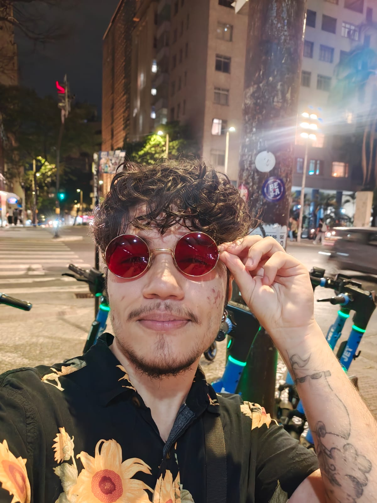 Me wearing round red sunglasses and a sunflower shirt on a city street at night